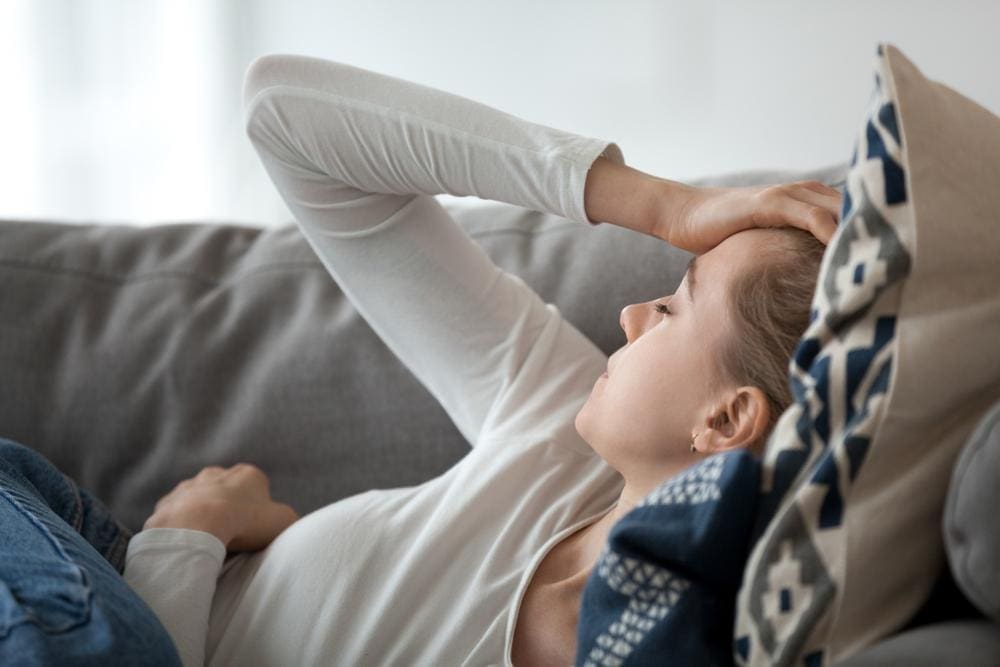 Young woman with cervicogenic headache lying on couch with hand on forehead.