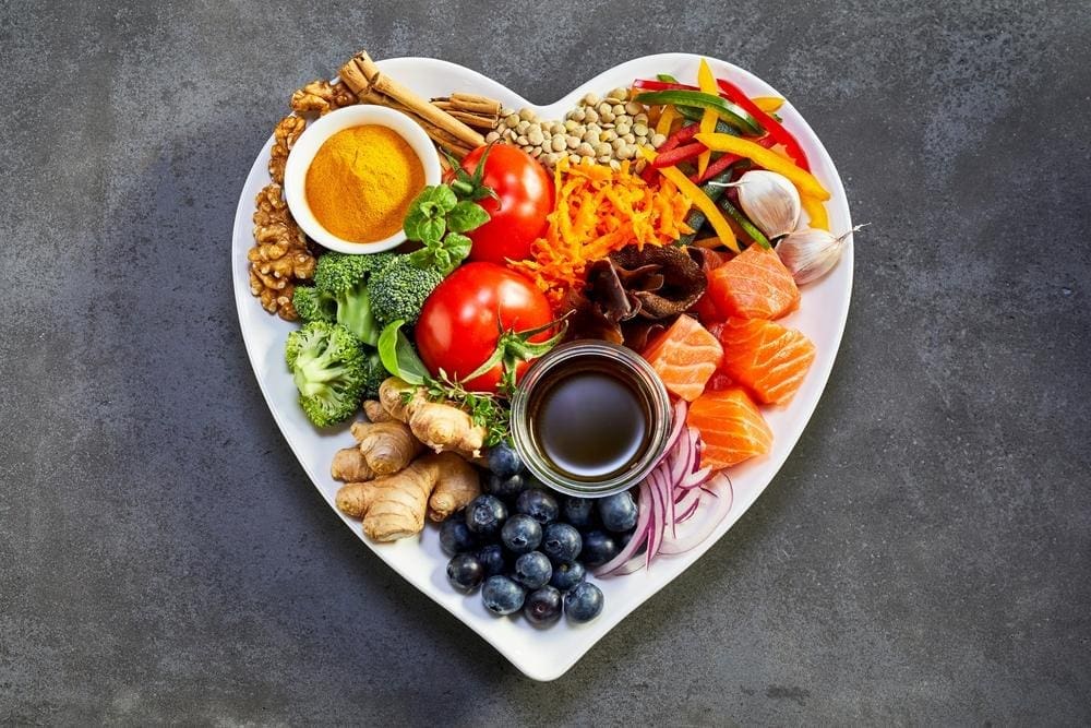 A heart shaped bowl of healthy produce, fish, fruit, vegetables and herbs.
