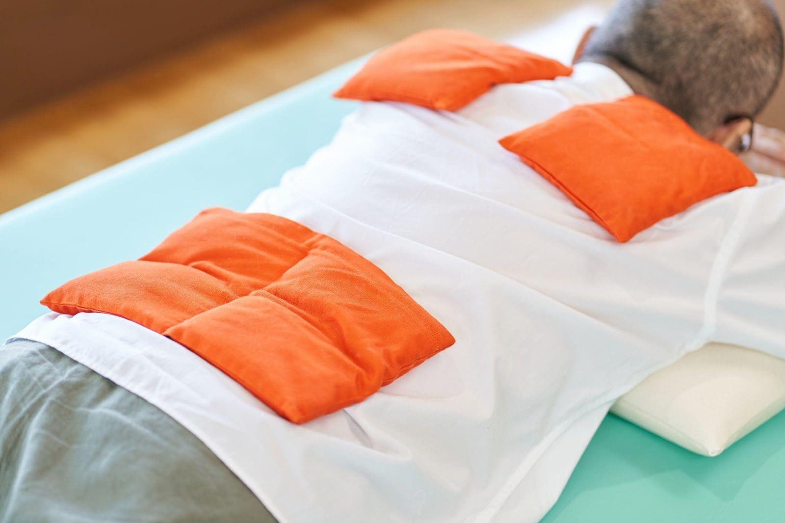Senior person lying on their stomach with heat packs on their back.
