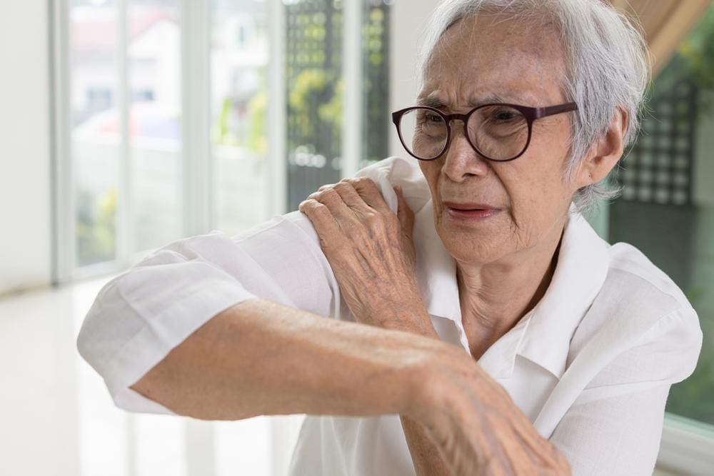 A woman is grasping her shoulder, in pain.