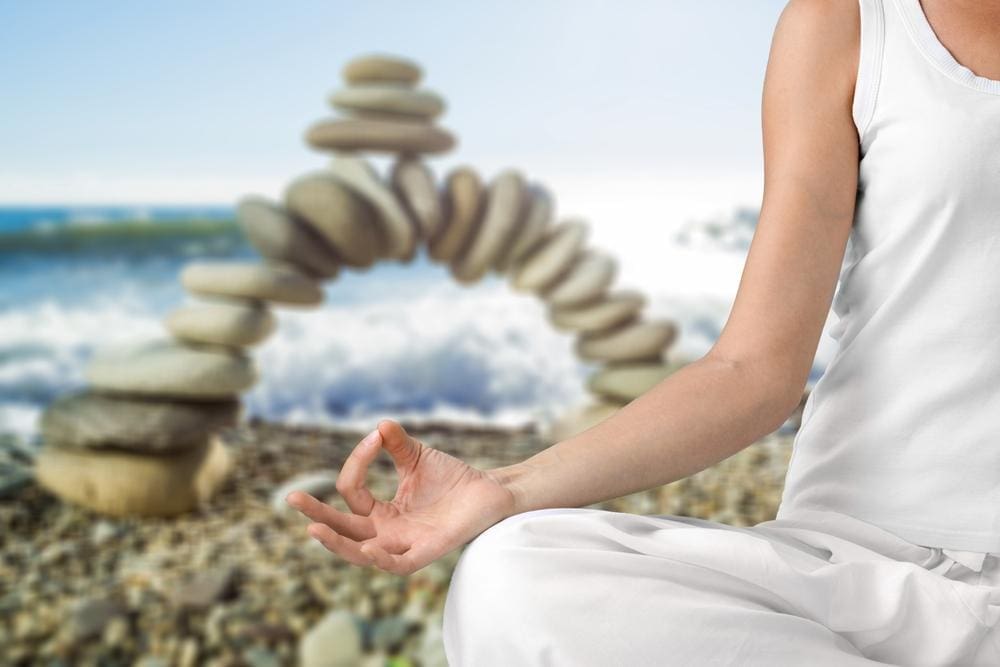 A young woman mediates outside in front of a rock arch.
