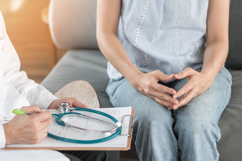 Doctor holding clipboard and stethoscope sitting down with patient.