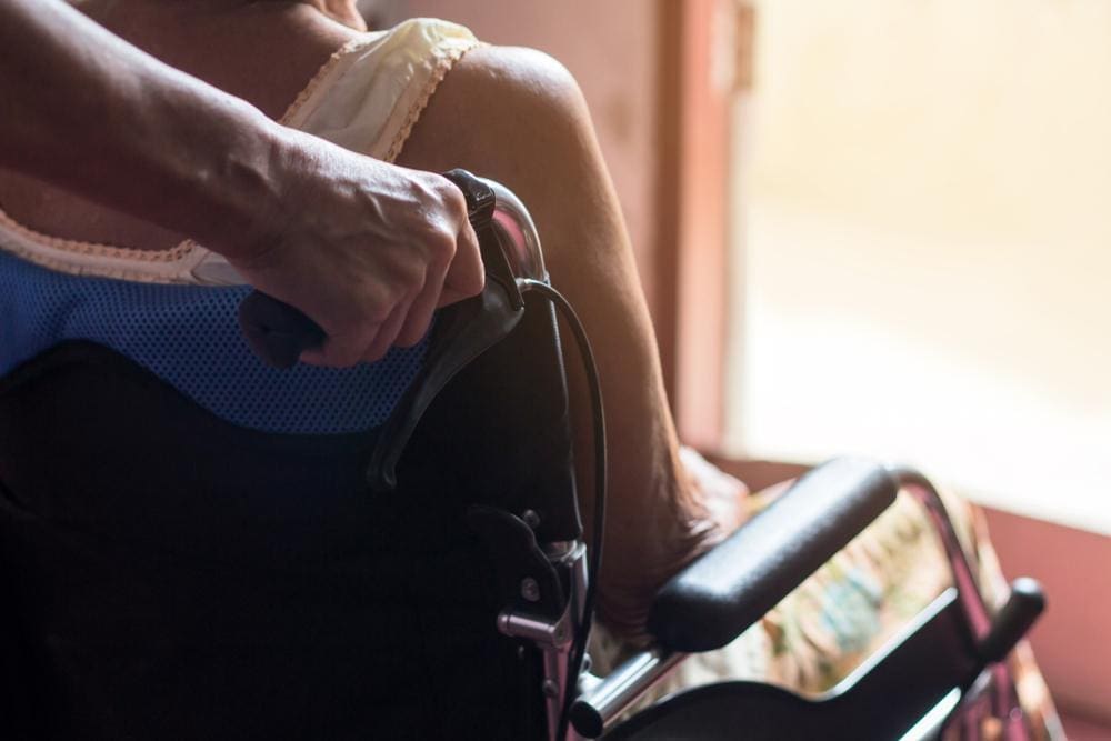 Woman in wheelchair looking out bright window.