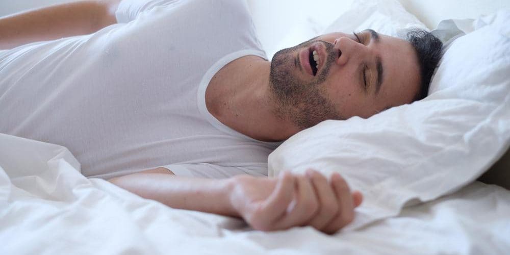 Man snoring while asleep in bed.
