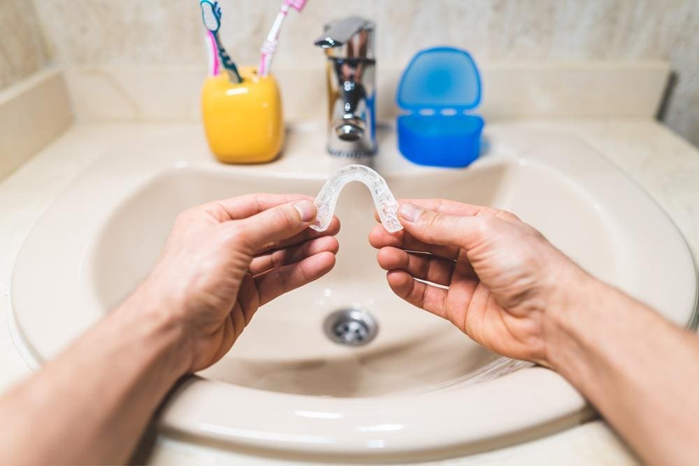 Man holding a dental mouth guard over the bathroom sink.