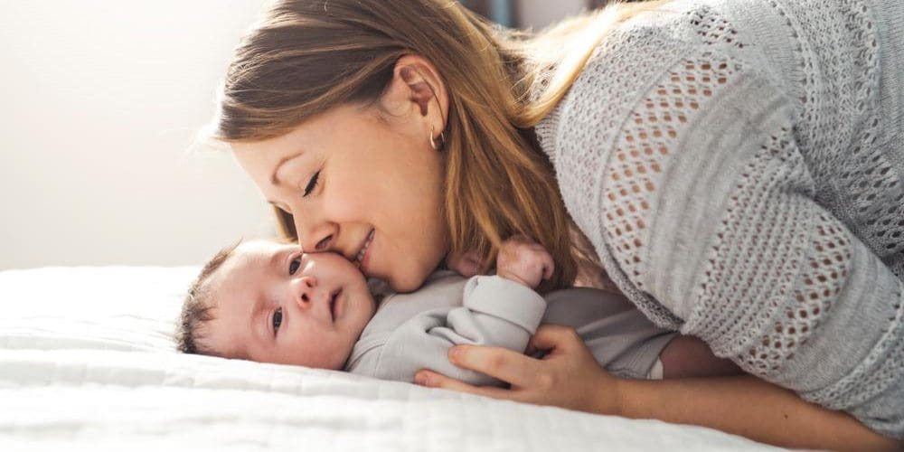 Mom snuggling newborn baby on soft blanket.