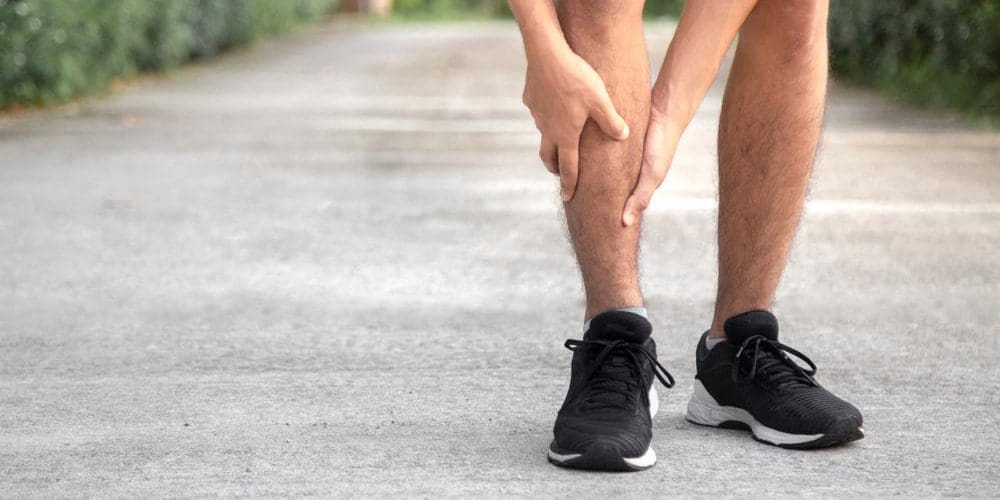 A man has stopped walking and his griping his shin.