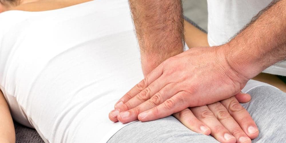 Chiropractor massaging tailbone area of patient lying facedown on treatment table.