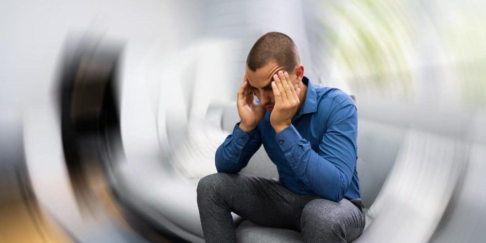 Man suffering from vertigo sitting down and holding his head.