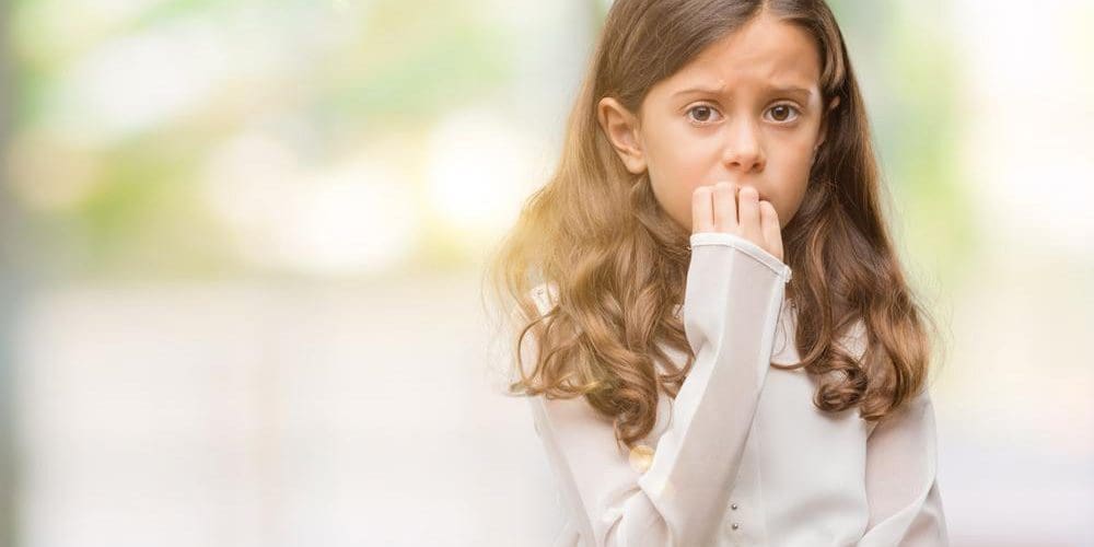 Young brunette girl biting her nails looking anxious.