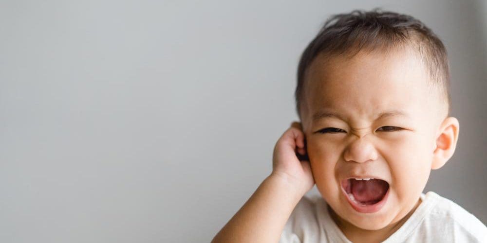 Toddler boy crying and tugging on his ear.