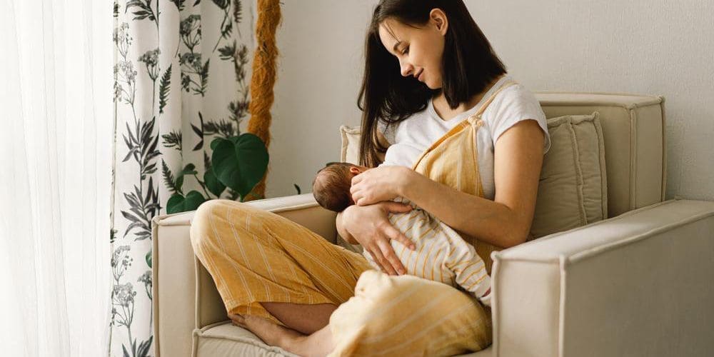 A young mother is sitting in a chair breastfeeding her baby.