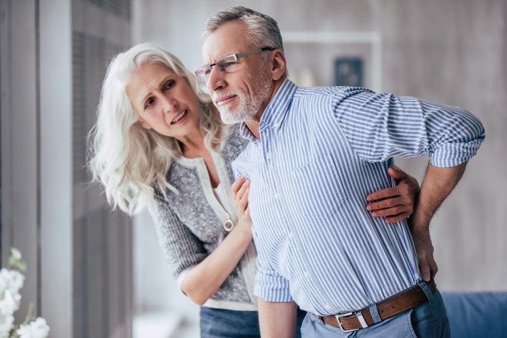 Older man with back pain walking with support from his wife.