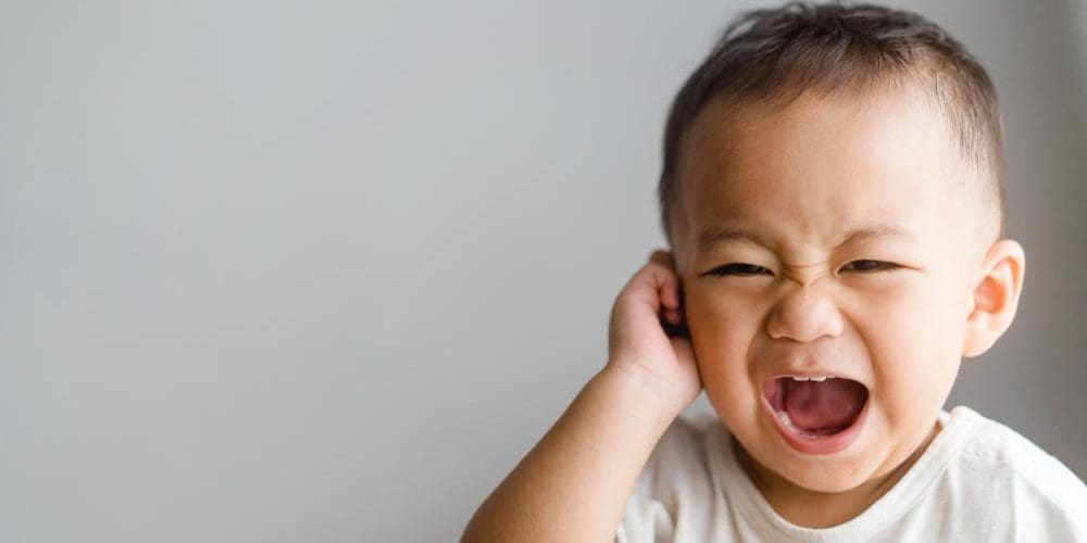 Toddler in pain holding his ear because of an ear infection.