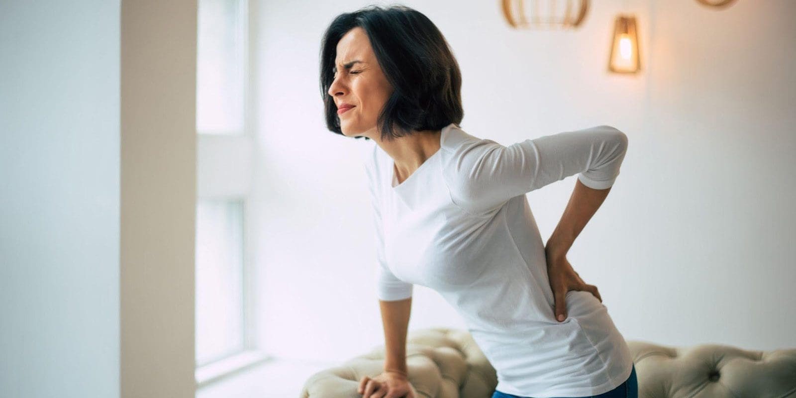 Middle age woman holding her lower back suffering from Spondylolisthesis pain.
