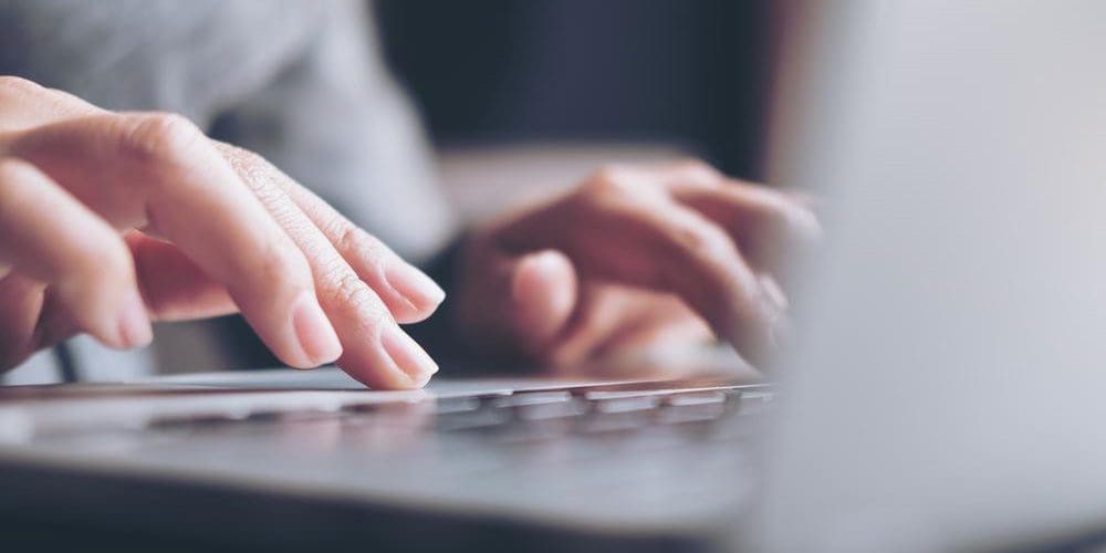 Closeup of a woman's hands typing on a keyboard.