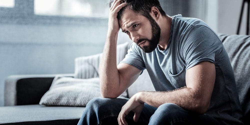 Anxious man sitting on a couch holding his head.