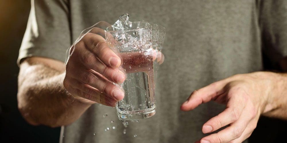 Man holds a glass of water while experiencing tremors.