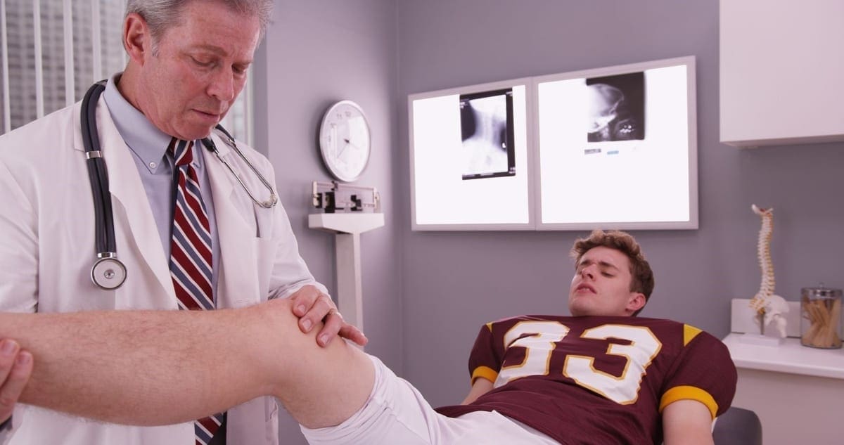 A chiropractor examines a football players knee injuries.