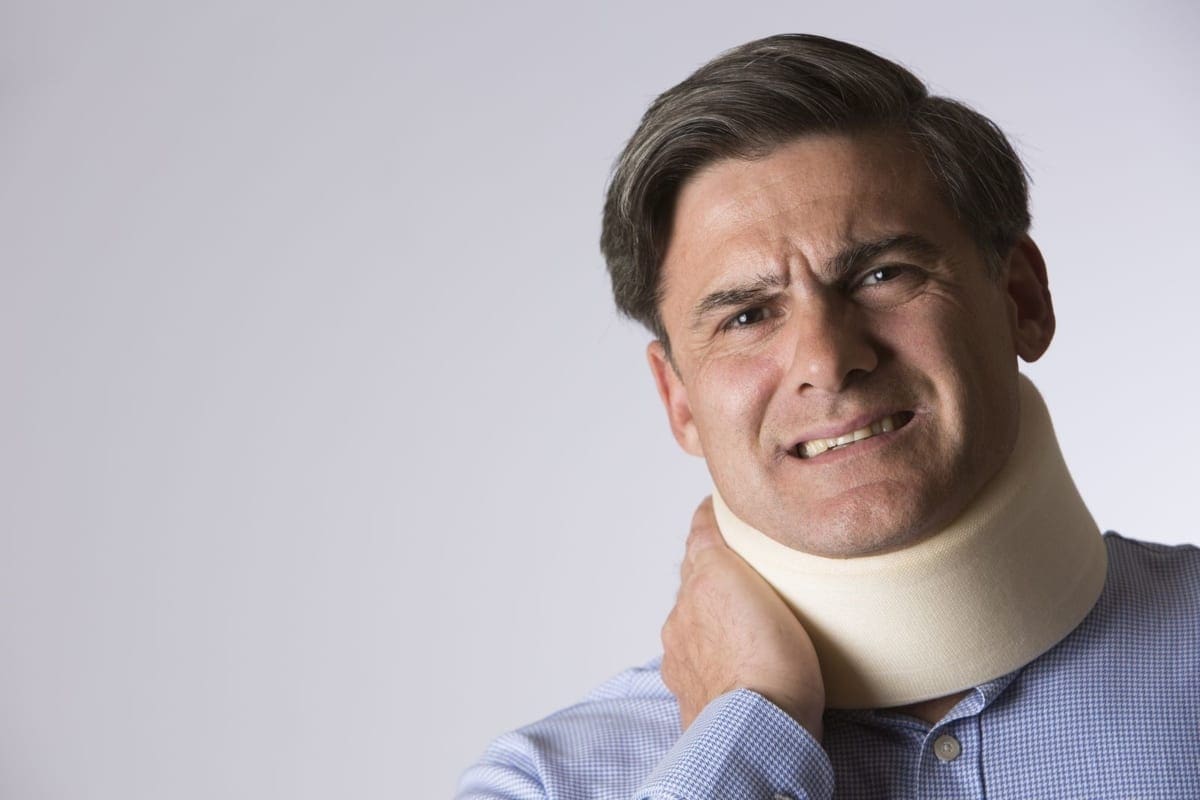 A man in a neck brace for whiplash winces in pain.