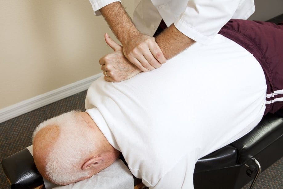 A chiropractor administers a spinal adjustment on a elderly man.