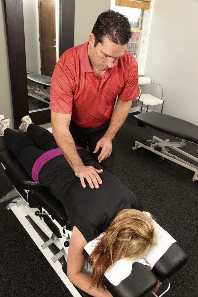 A woman is laying on a chiropractic adjustment table for spinal manipulation treatment.