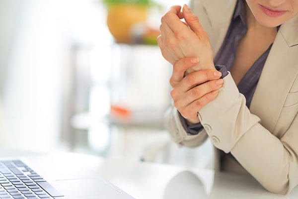A woman is experiencing wrist pain at work while sitting in front a keyboard.