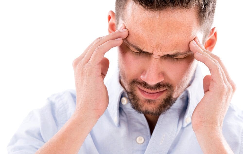 A man is wincing and holding his temples because of headache pain.
