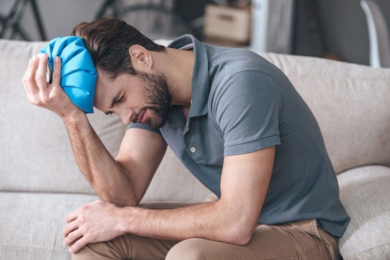 A man holds an icepack on his forehead because he has a very bad headache.