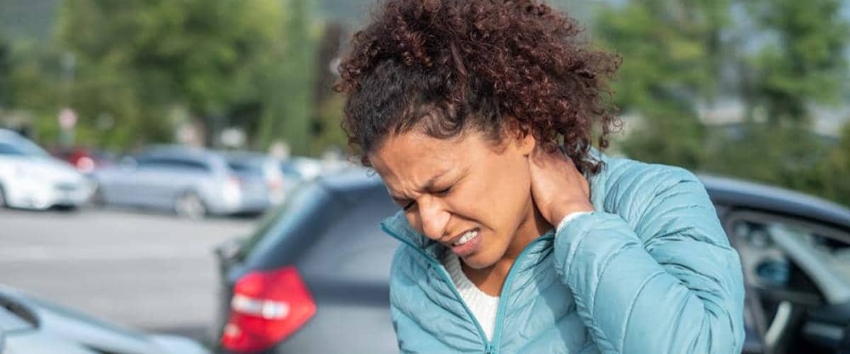 A woman clutches the back of her neck in pain after a rear-end car accident.