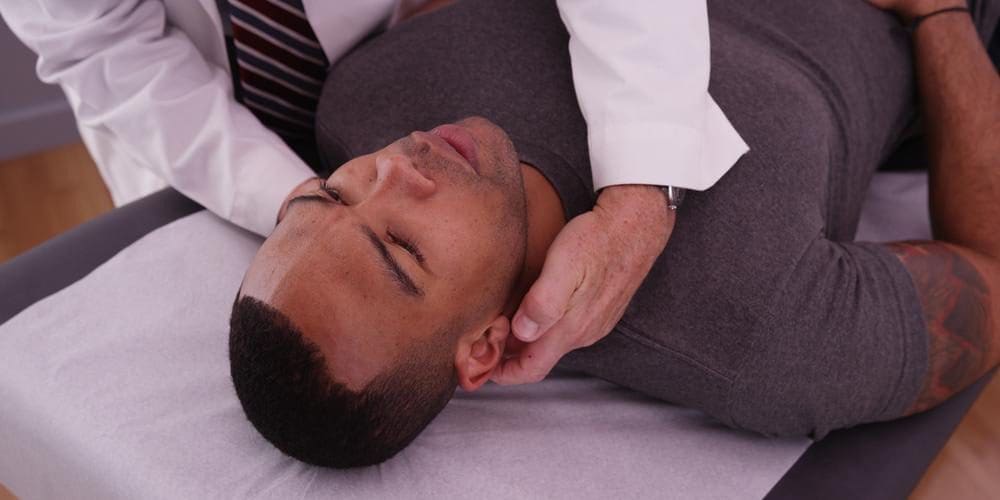 A man is being treated by a chiropractor to ease symptoms of a brain injury.
