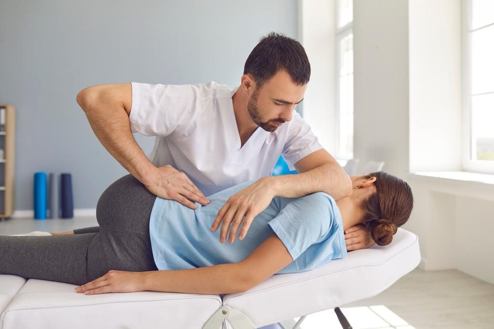 A chiropractor is treating a woman for back pain caused by bad posture. 