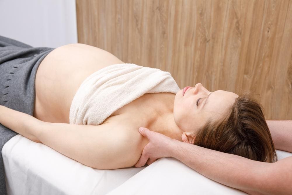 A pregnant woman is getting chiropractic treatment to alleviate back pain.