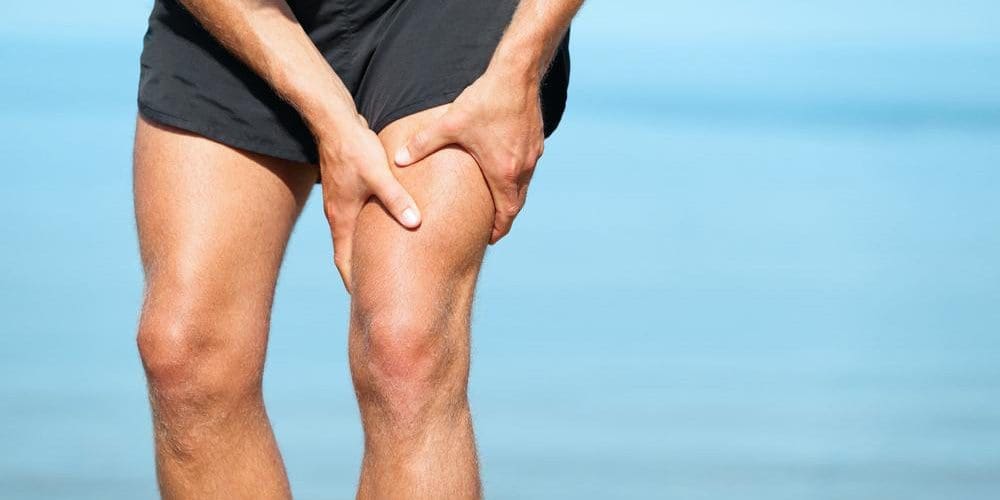A man in running shorts is grasping his thigh because he tore a muscle.