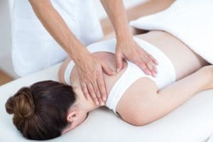 Chiropractor treating the upper middle back of woman laying face down on table.