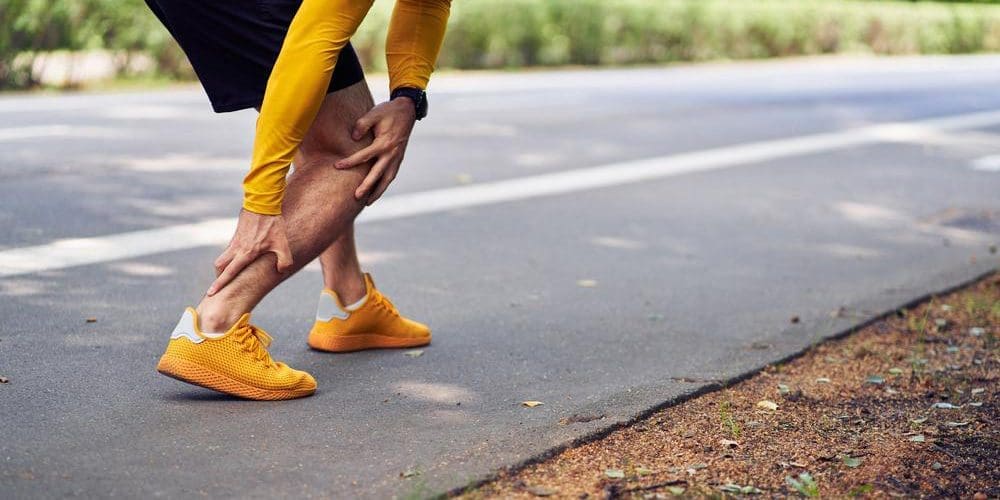 A runner has stopped and his grasping his ankle because he has achilles tendonitis.
