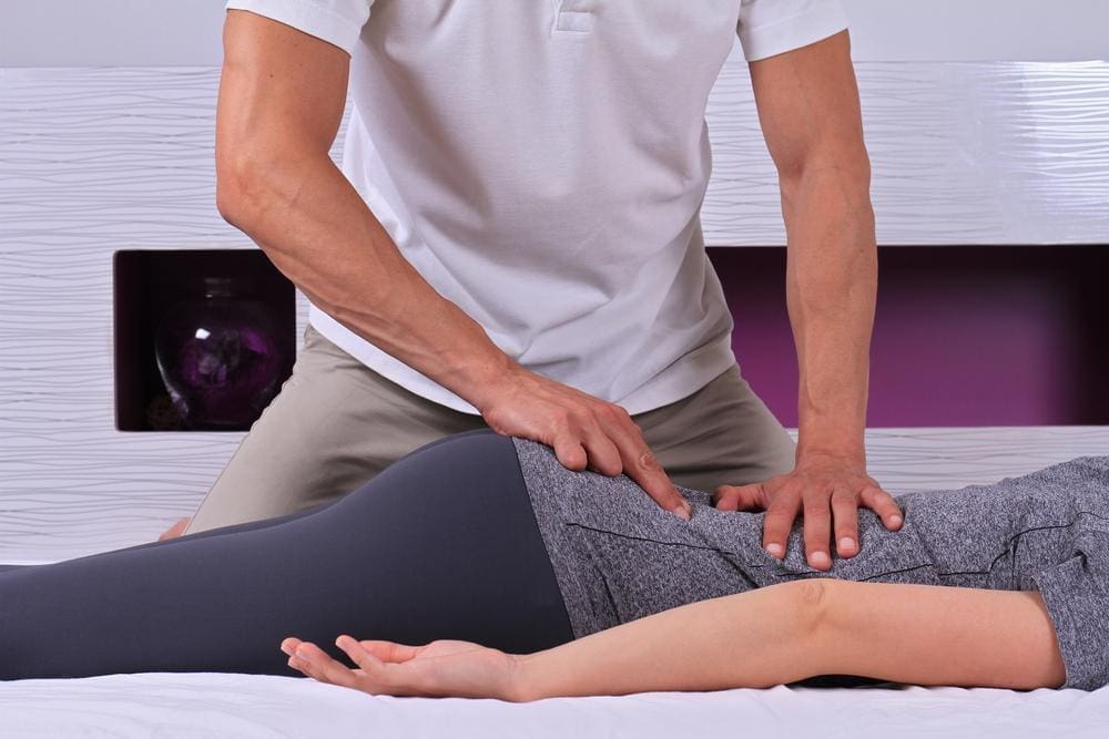 Chiropractor adjusting lower back of female patient, to help alleviate constipation. 