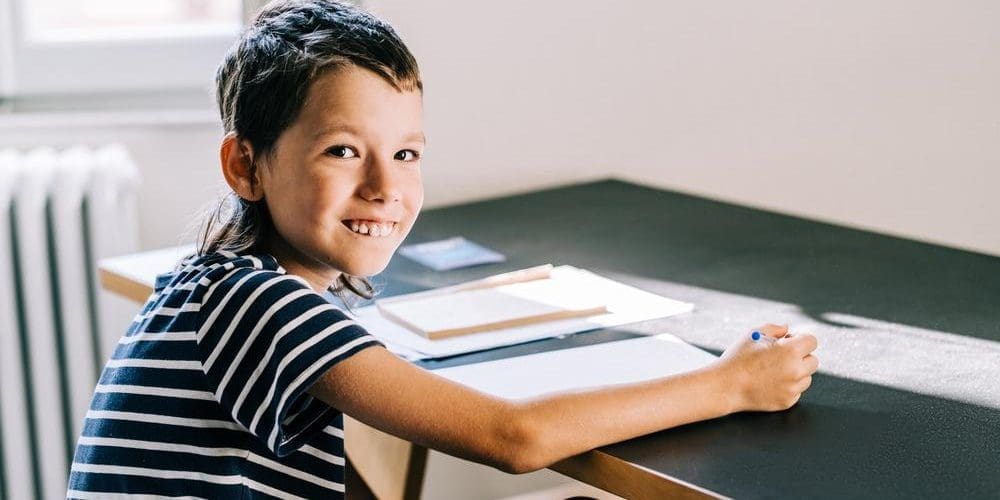 Young boy with autism sitting at desk writing in notebook.