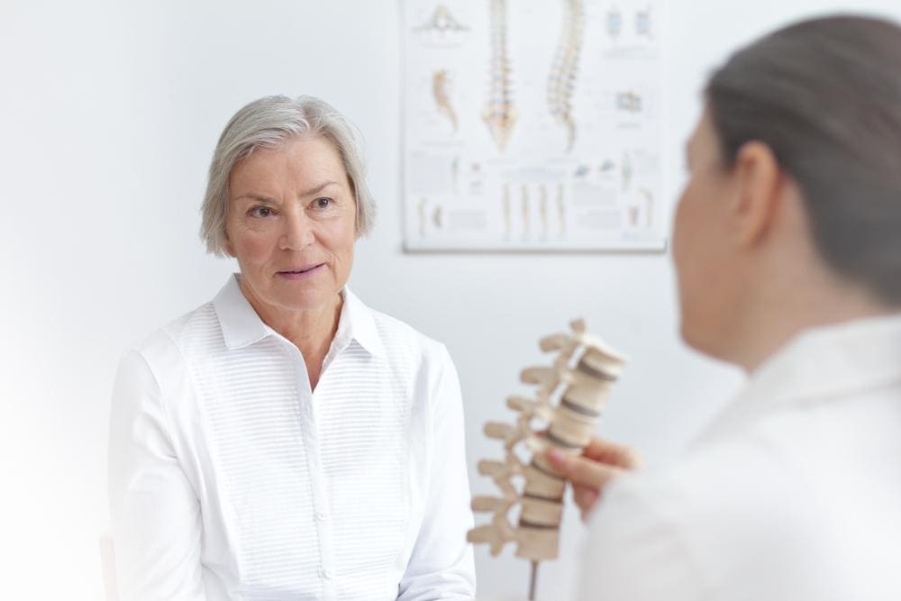 Chiropractor showing model of spine to senior female patient.
