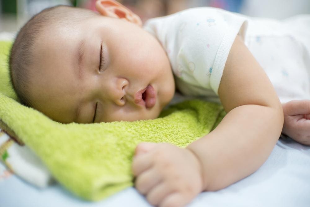 Young baby sleeping peacefully on green blanket.
