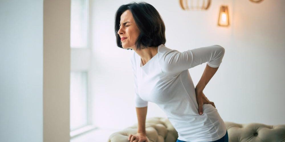 Woman standing up from sofa holding her lower back in pain.