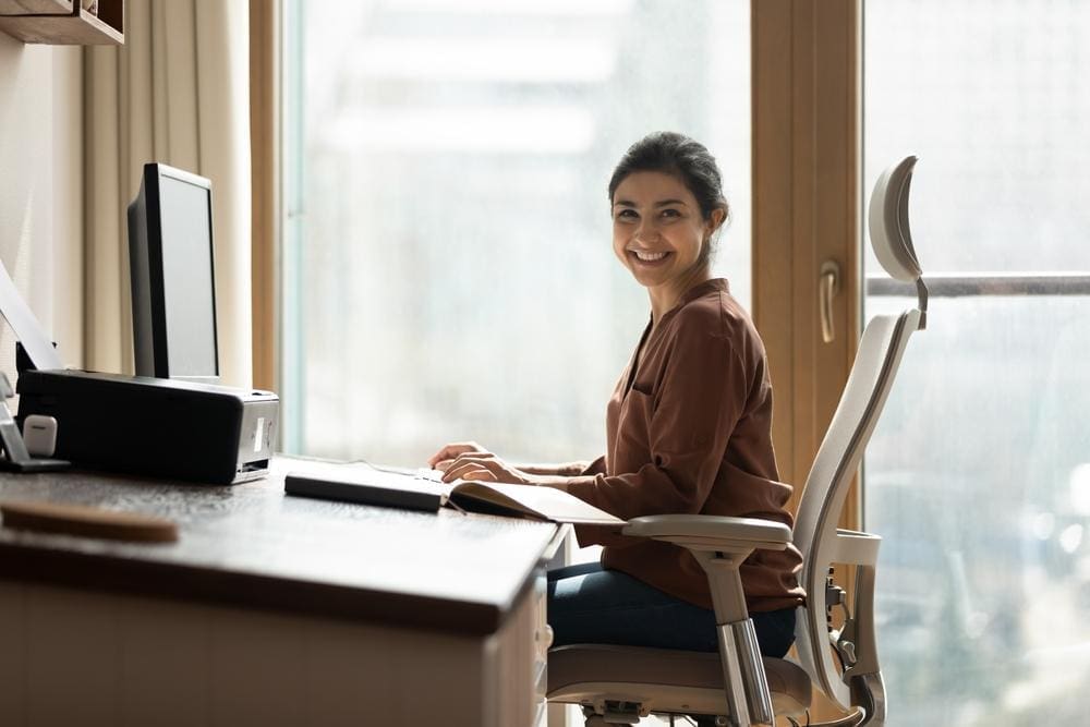 Smiling woman sitting up straight in ergonomic office chair.
