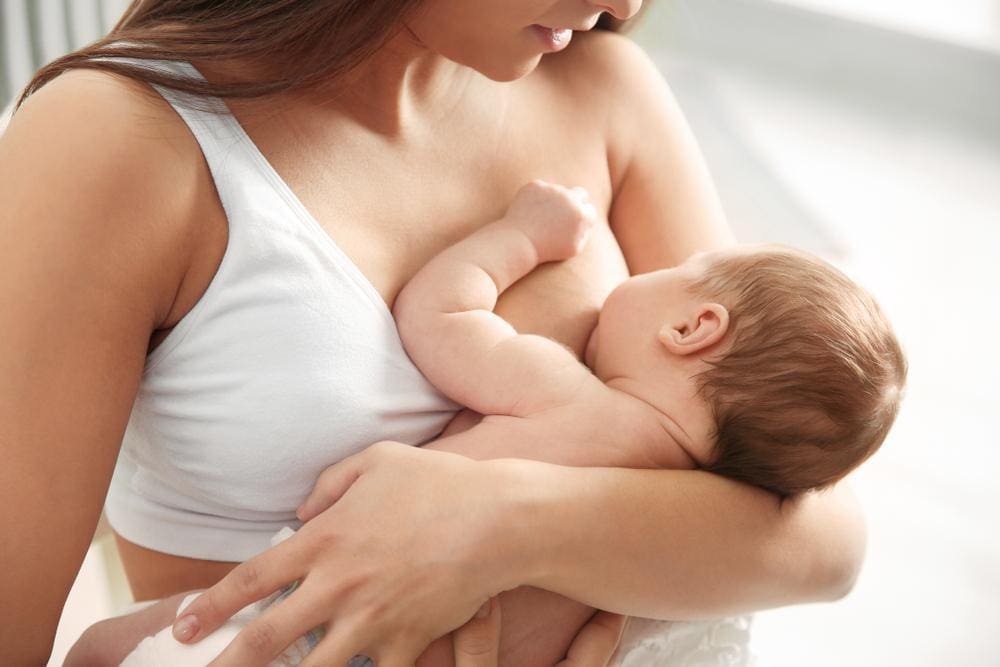 Young mother wearing a white nursing bra breastfeeds her newborn.