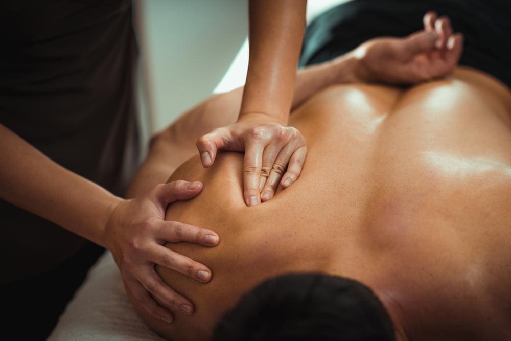 Chiropractor massaging male patient's shoulder.
