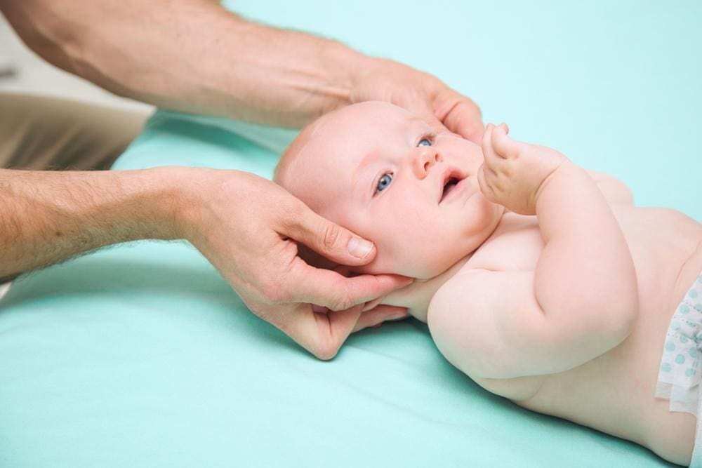 Chiropractor's hands adjust a six-month-old baby's neck.