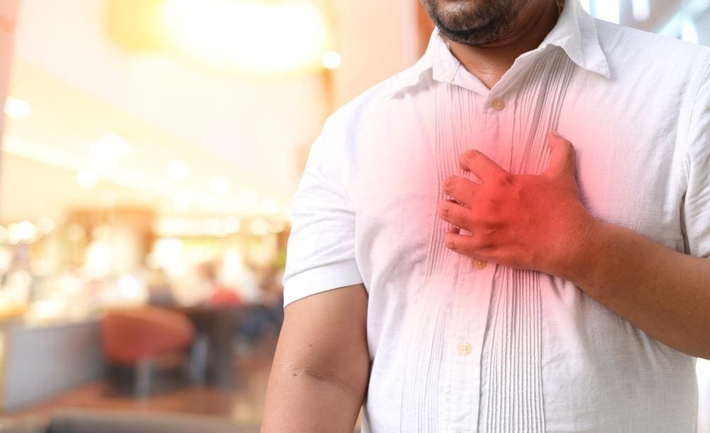 Young man with hand on his chest experiencing heartburn.