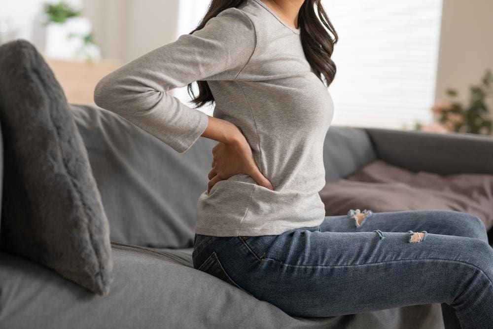 Woman sitting on the edge of a couch stretching her back.
