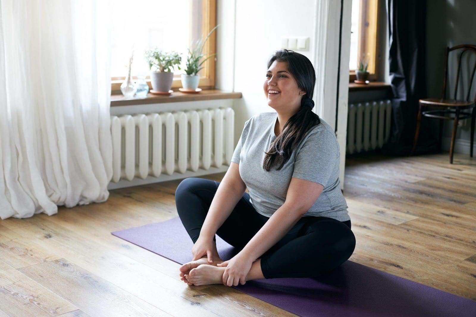 Young woman sitting on exercise mat in living room.
